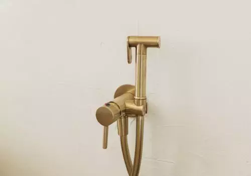 Stylish brass bidet shower on wall, modern bathroom design detail close up.Handle water sprayer, bathroom interior element. Hygiene concept